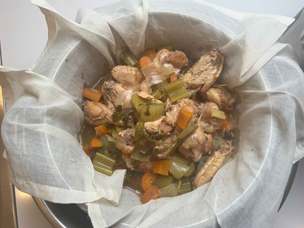 Straining homemade chicken stock through cheesecloth into a bowl